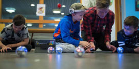 A teacher and student on the floor, testing a Sphero robot