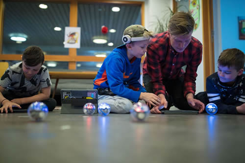 A teacher and student on the floor, testing a Sphero robot