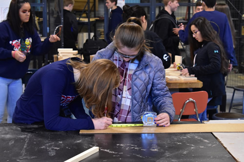 Two female students measuring wood and working on a project.