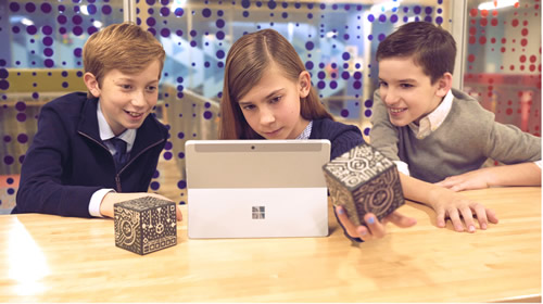 3 young students eagerly looking at a MERGE Cube, an AR app, with a laptop