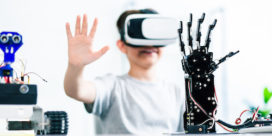 Selective focus of robotic humanoid hand standing on the table while a smart boy testing it while using VR glasses