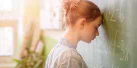a young girl banging her head against the blackboard in anguish