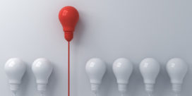 A red light bulb floats above plain light bulbs illustrating design thinking and makerspaces.