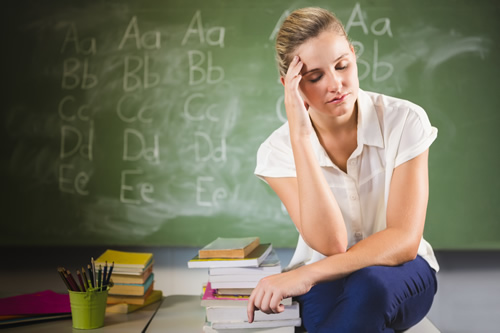 A female teacher sits in her classroom and is frustrated--it's important to support struggling teachers.