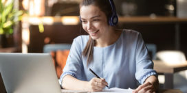 A woman on a laptop with headphones is watching a webinar, showing how personalized PD for teachers can be very convenient.