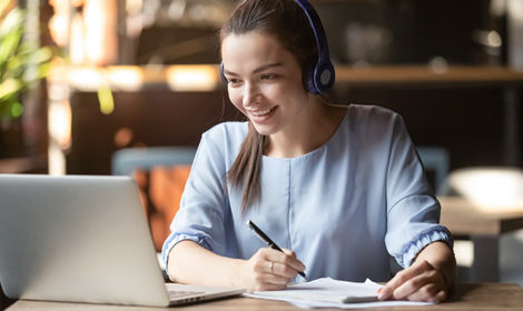 A woman on a laptop with headphones is watching a webinar, showing how personalized PD for teachers can be very convenient.