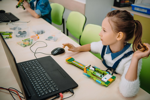 A young girl learns coding at a computer as she uses a robot, showing why robots for K-12 are important.