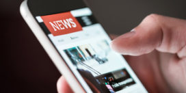 A hand holding a smartphone screen with a news site demonstrates how teens get their media on the go.