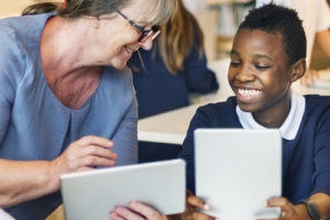 Research shows English learners and students of color are underrepresented in advanced classes--but key strategies can boost their enrollment, like this student smiling using a tablet with a teacher.