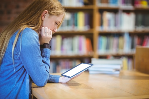 A report takes a look at some of the digital learning tools and strategies shaping the next calendar year, like this student sitting in the library with a tablet.