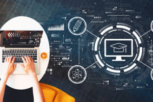 A person sits on a chair working on a laptop on a white table, doing online learning.